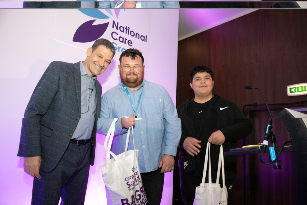Three men stood on a stage, two holding goody bags